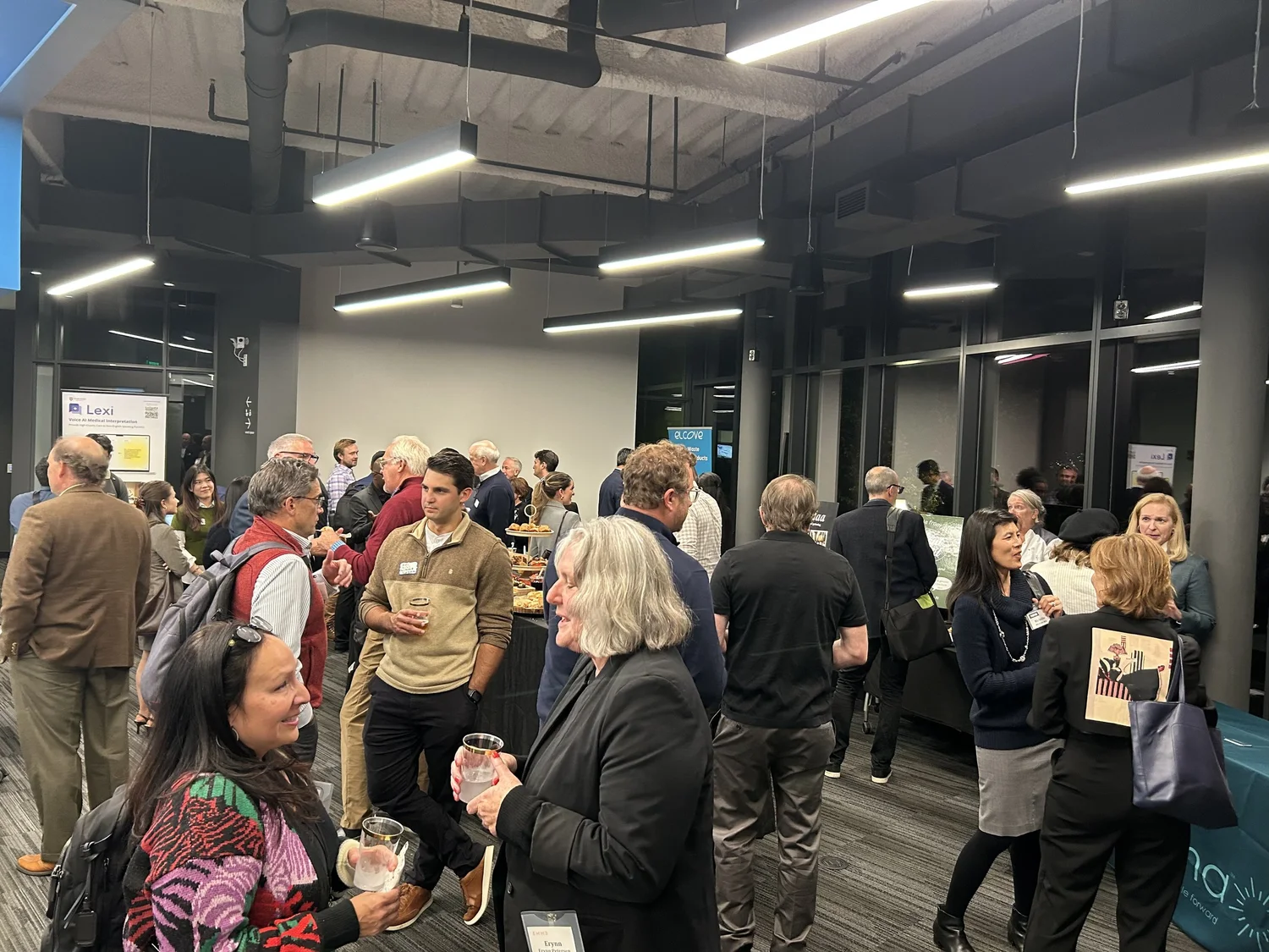 People attending a networking event in an indoor space, with some looking at exhibits and engaging in conversations.
